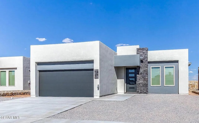 contemporary home with concrete driveway, stone siding, an attached garage, and stucco siding