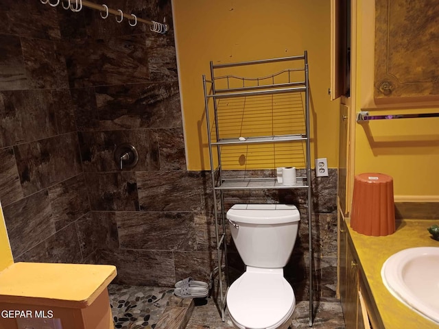 bathroom featuring tiled shower, vanity, toilet, and tile walls