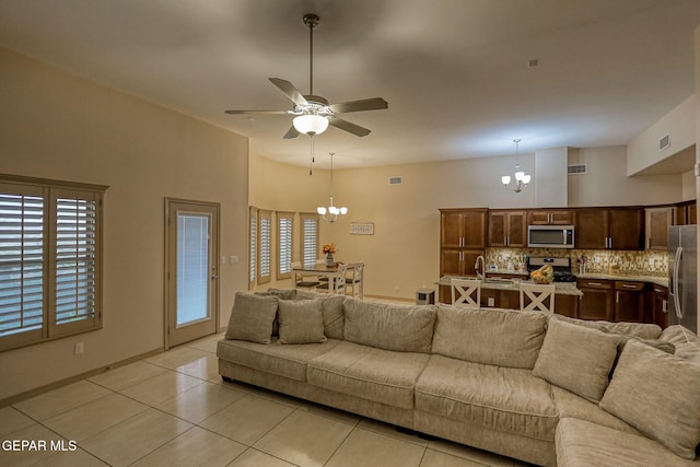 tiled living room with ceiling fan with notable chandelier and a high ceiling