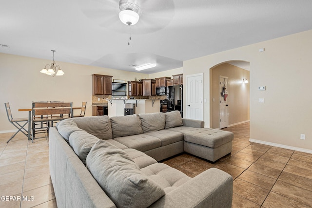 tiled living room with ceiling fan with notable chandelier