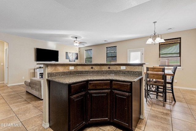 kitchen with dark brown cabinetry, a kitchen island, pendant lighting, light tile patterned flooring, and ceiling fan with notable chandelier