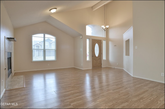 foyer entrance with vaulted ceiling with beams, a tile fireplace, a chandelier, and light hardwood / wood-style flooring