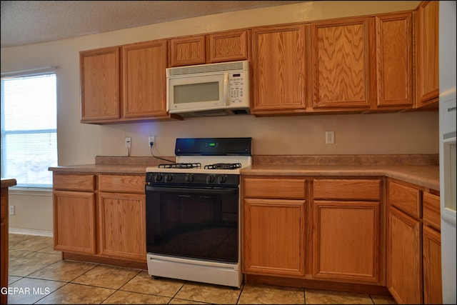 kitchen featuring a textured ceiling, light tile patterned floors, and white appliances