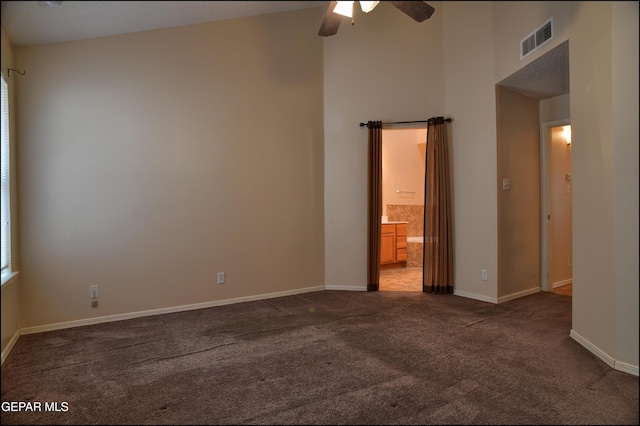 carpeted empty room featuring ceiling fan and a high ceiling