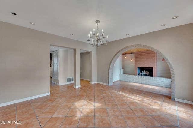 empty room featuring light tile patterned floors, a brick fireplace, and a notable chandelier