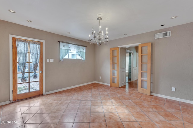 tiled spare room featuring an inviting chandelier and french doors