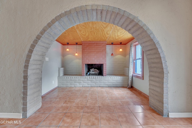 unfurnished living room featuring tile patterned floors, ornamental molding, wood ceiling, and a brick fireplace