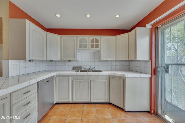 kitchen with backsplash, stainless steel dishwasher, sink, light tile patterned floors, and tile countertops