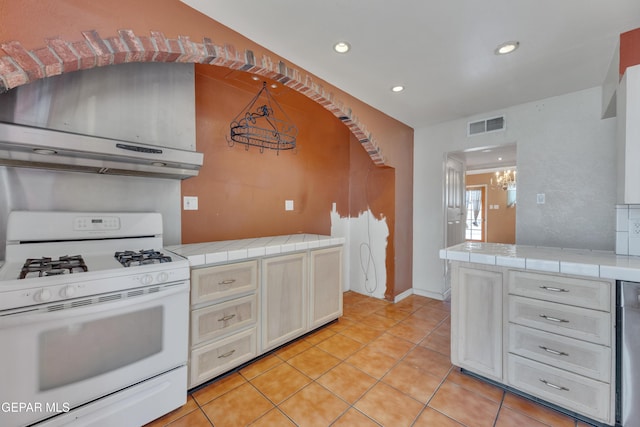 kitchen featuring white gas range, exhaust hood, tile countertops, an inviting chandelier, and light tile patterned flooring