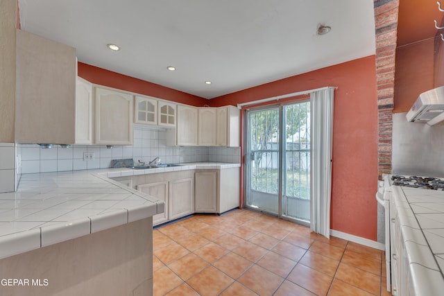 kitchen with decorative backsplash, gas range gas stove, sink, light tile patterned floors, and tile counters