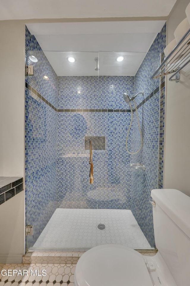 bathroom with tile patterned floors, toilet, a shower with door, and tile walls