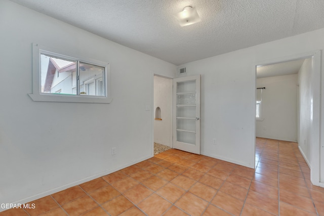 tiled empty room featuring a textured ceiling