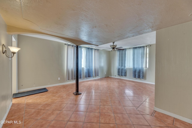 basement featuring light tile patterned floors, a textured ceiling, and ceiling fan