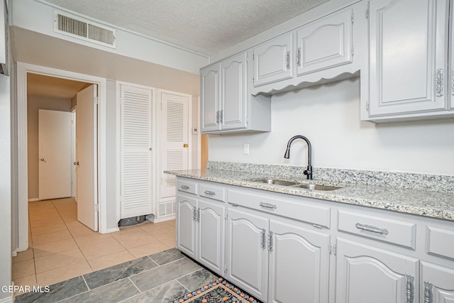 kitchen featuring light tile patterned floors, visible vents, light stone countertops, a textured ceiling, and a sink