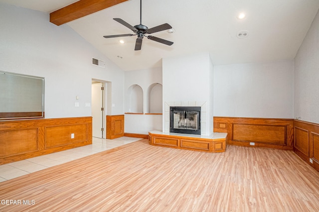 unfurnished living room featuring beam ceiling, light wood finished floors, visible vents, a tiled fireplace, and wainscoting