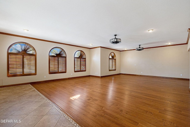 empty room with ceiling fan, ornamental molding, a textured ceiling, and light wood-type flooring