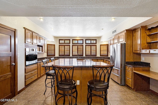 kitchen with light tile patterned flooring, a textured ceiling, appliances with stainless steel finishes, a kitchen island, and a breakfast bar area