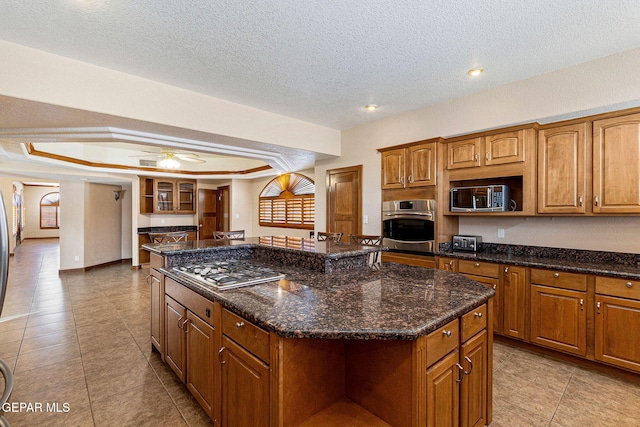 kitchen featuring a raised ceiling, ceiling fan, a textured ceiling, a kitchen island, and stainless steel appliances