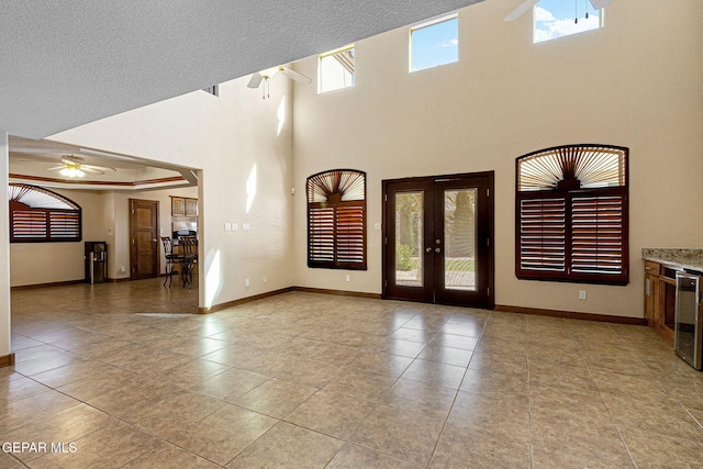 tiled empty room with ceiling fan, french doors, a towering ceiling, and a healthy amount of sunlight