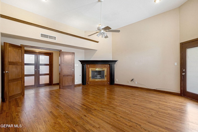 unfurnished living room with hardwood / wood-style floors, ceiling fan, high vaulted ceiling, and french doors