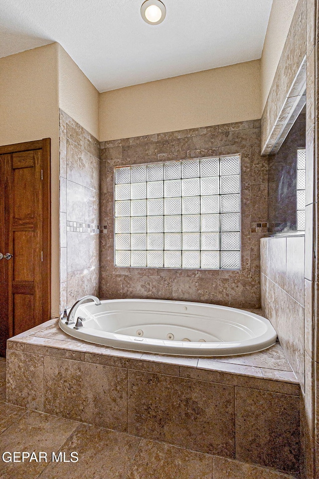 bathroom with a relaxing tiled tub, a healthy amount of sunlight, and tile walls