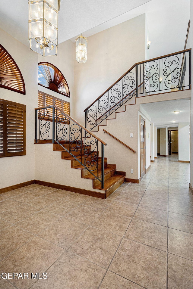 stairs with tile patterned flooring, a towering ceiling, and a chandelier