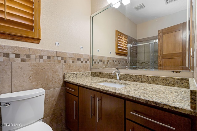 bathroom featuring vanity, toilet, tile walls, and a shower with shower door