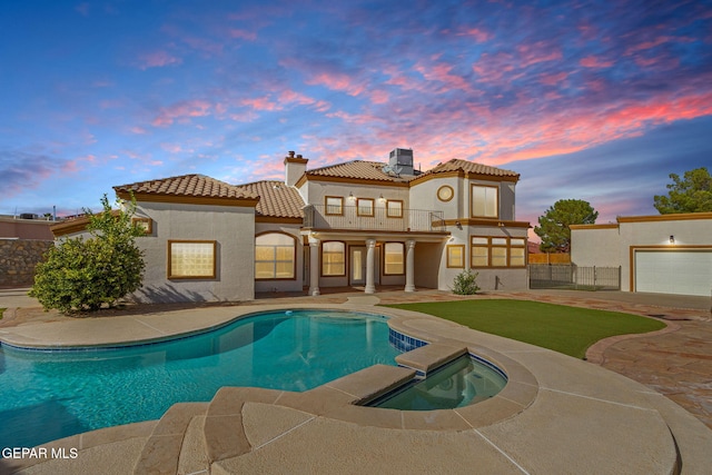 back house at dusk featuring a pool with hot tub, a patio area, and a balcony