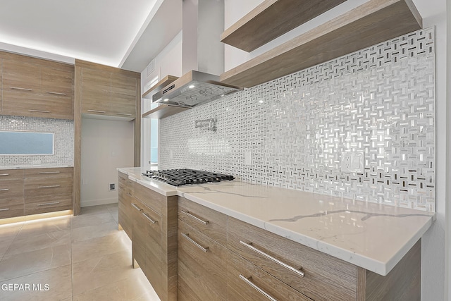 kitchen with wall chimney range hood, stainless steel gas cooktop, light stone counters, backsplash, and light tile patterned floors