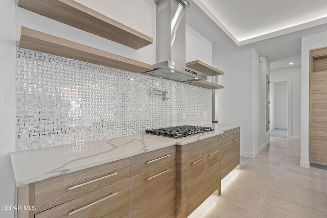 kitchen featuring light stone countertops, wall chimney exhaust hood, stainless steel gas cooktop, backsplash, and light tile patterned floors