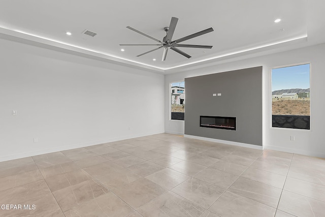 unfurnished living room featuring a tray ceiling, ceiling fan, and light tile patterned floors