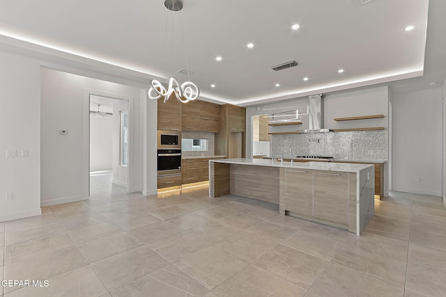 kitchen with decorative backsplash, stainless steel oven, built in microwave, a large island with sink, and decorative light fixtures