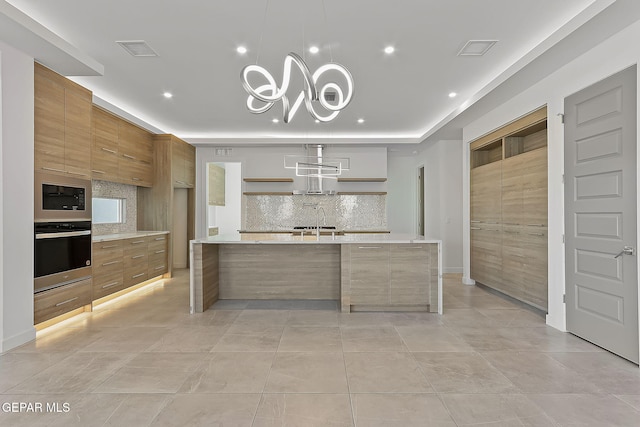 kitchen featuring decorative backsplash, stainless steel oven, built in microwave, sink, and a large island with sink