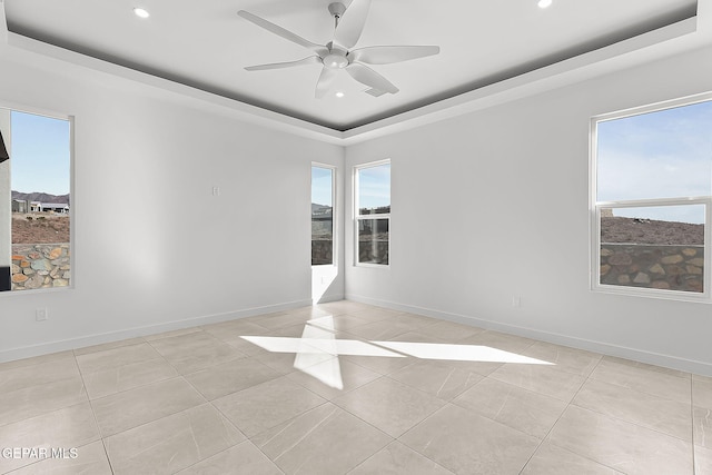 tiled empty room featuring ceiling fan and a tray ceiling