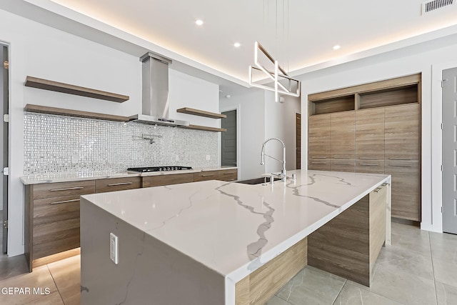 kitchen featuring light stone countertops, a spacious island, wall chimney range hood, sink, and decorative light fixtures