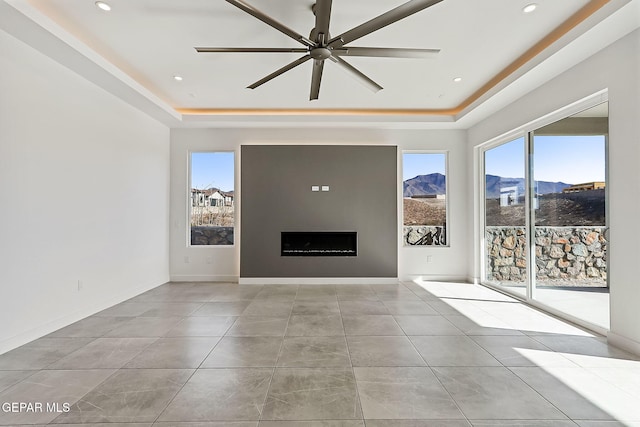 unfurnished living room featuring a mountain view, light tile patterned floors, a tray ceiling, and ceiling fan