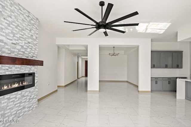 unfurnished living room featuring ceiling fan with notable chandelier and a tiled fireplace