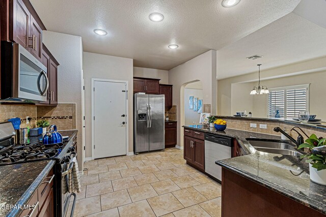 kitchen featuring a notable chandelier, sink, appliances with stainless steel finishes, and dark stone counters