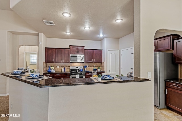 kitchen featuring appliances with stainless steel finishes, a textured ceiling, a center island, and backsplash