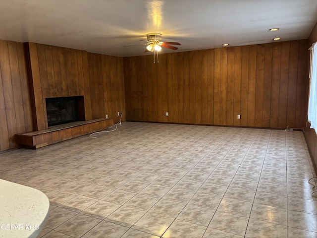 unfurnished living room featuring ceiling fan, a large fireplace, and wooden walls