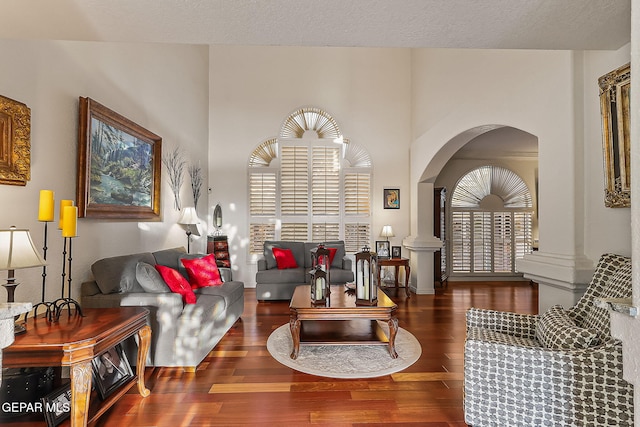 living room with plenty of natural light, dark hardwood / wood-style floors, ornate columns, and a textured ceiling