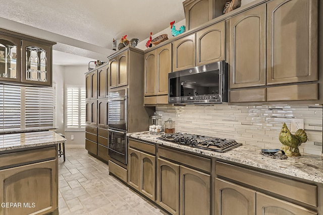 kitchen featuring backsplash, light stone counters, and stainless steel appliances