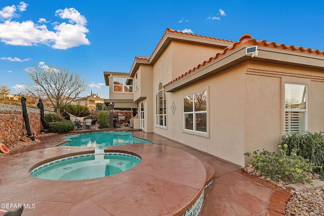 rear view of property with a patio and a pool with hot tub