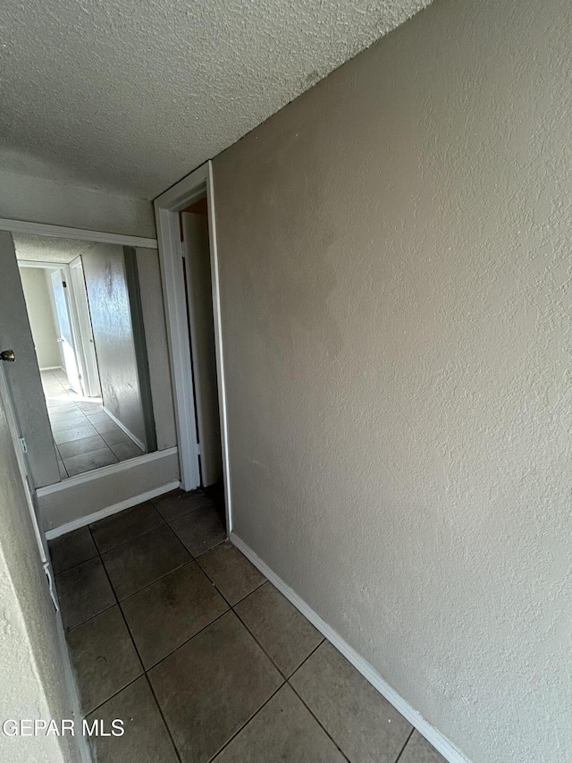 hallway featuring a textured ceiling and dark tile patterned floors