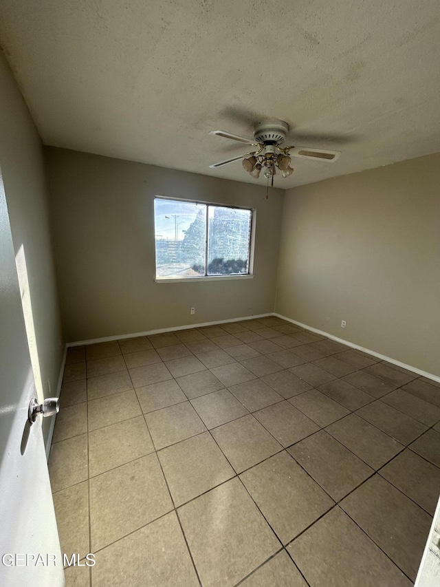 empty room with ceiling fan, light tile patterned flooring, and a textured ceiling