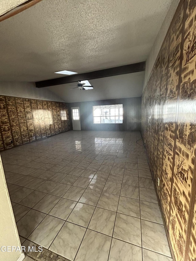 spare room with lofted ceiling with beams, ceiling fan, and a textured ceiling