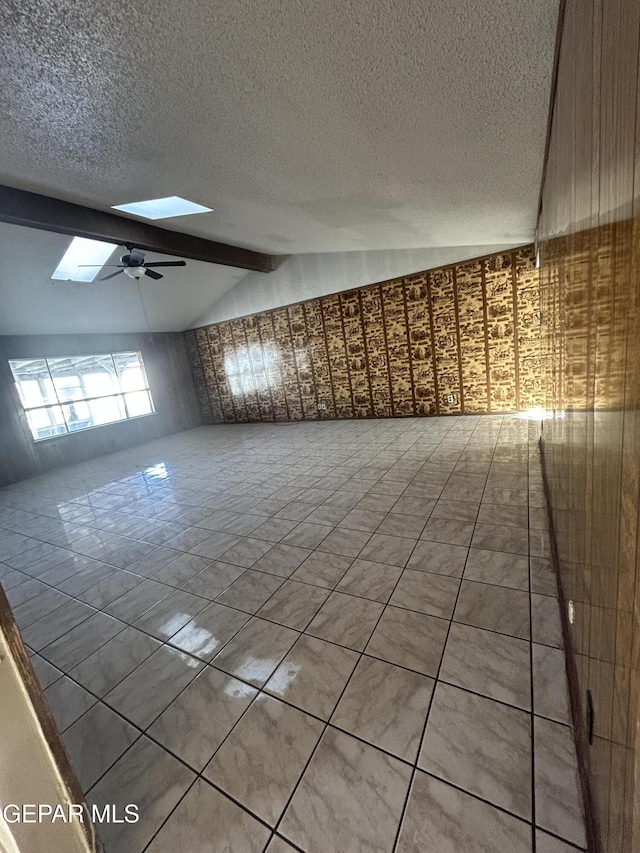 unfurnished room featuring a textured ceiling, ceiling fan, and vaulted ceiling with skylight