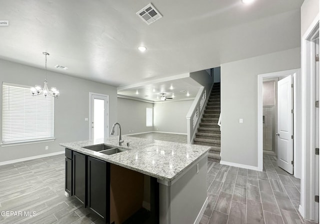 kitchen featuring light stone counters, sink, decorative light fixtures, light hardwood / wood-style flooring, and a center island with sink