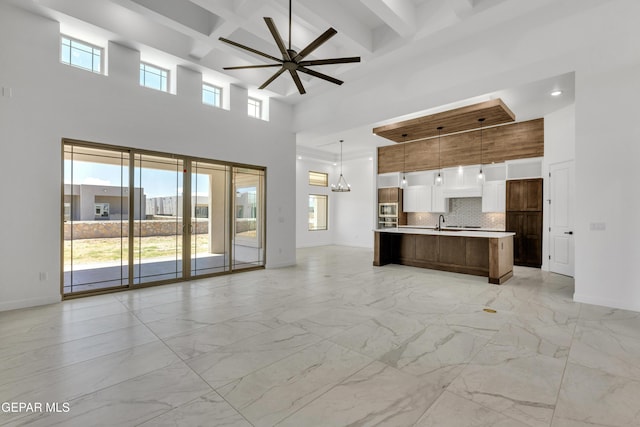 unfurnished living room featuring a towering ceiling, coffered ceiling, ceiling fan, sink, and beamed ceiling