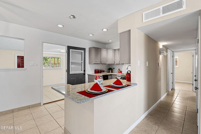 kitchen featuring kitchen peninsula, light tile patterned floors, tasteful backsplash, and gray cabinets